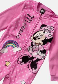 Vaaleanpunainen fleece-yksiö, jossa on valkoisia pisteitä, suuri Minnie Mouse -grafiikka, värikäs sateenkaari ja tähtiaktsentit. Vetoketjusuljenta edessä.