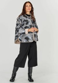 Hallitusjakke hallis musta lillemustriga, kerge kangas, nööbiga disain, beež äär. Kombineeritud mustade laia säärega pükste ja pikkade saabastega.