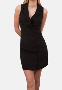 Robe noire sans manches avec un col en V, fermeture à bouton sur le devant et une coupe ajustée. Tissu lisse et longueur au genou.