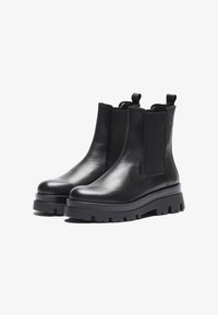 Botas de tobillo de cuero negro con paneles laterales elásticos y tira de agarre, con una suela gruesa para mayor agarre y altura.