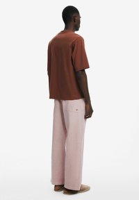 T-shirt en coton marron à manches courtes, associé à un pantalon en lin rose clair. Coupe ample et palette de couleurs neutres. Design simple.