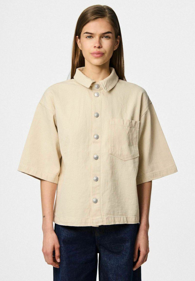 Bežna oversized kratka majica s kratkimi rokavi, izdelana iz teksturirane tkanine, z ovratnikom, sprednjim žepom in srebrnimi pritisnimi gumbi po sredini.