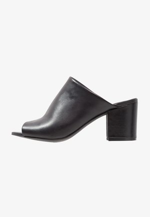 Musta nahka avoimen varvastyylinen malli, jossa on tyylikäs muotoilu, paksut lohkosaappaat ja sileä pinta, korostaen minimalistista tyyliä.