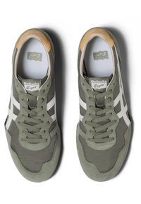 Zelené sportovní boty s bílými pruhy, vyrobené z semišového a síťovinového materiálu, s texturovanými šněrovadly a akcentem světle hnědé barvy na patě. Na jazyku se nachází logo.