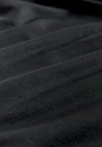 Fekete szövet lágy textúrával, gyűrött megjelenéssel. A felületen finom fény- és árnyjáték figyelhető meg.