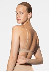 Bleke bralette met verstelbare bandjes, gladde stof en minimalistisch ontwerp. De hand van het model rust op de onderrug, wat de stijl benadrukt.