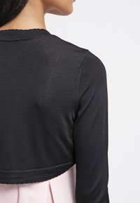 Svart, ribbad, kortärmad tröja med rund halsringning, strukturerad tyg och utan knäppningar, parat med en ljusrosa, plisserad klänning under.