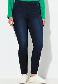 Granatowe legginsy jeansowe z elastycznym pasem, zaprojektowane dla komfortu, charakteryzujące się zwężanymi nogawkami i bocznymi kieszeniami. Uzupełnione białymi trampkami.