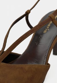 Sandal à talons haut en suède marron avec des brides croisées et un talon en bois. Semelle intérieure lisse et polie avec des détails de marque.