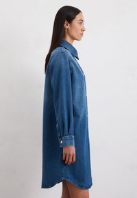 Jeanshemdkleid in Mittelblau mit durchgehender Knopfleiste, Kragen und langen Ärmeln mit Manschettendetails. Länge bis zur Mitte des Oberschenkels mit abgerundetem Saum.