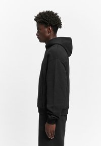 Black hoodie with a drawstring hood, ribbed cuffs, and a front pouch pocket. Made of soft fabric, it features a relaxed fit and minimalistic design.