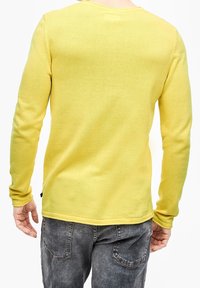 Maglione giallo a maniche lunghe con un design a maglia testurizzata. Presenta un collo rotondo ed è abbinato a jeans in denim grigi.