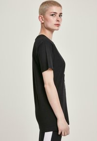 Sort bomulds-T-shirt med korte ærmer, der har en afslappet pasform og et enkelt design, båret med sorte bukser med hvide sidelister.