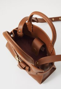 Borsa in pelle marrone con parte superiore arrotondata, doppio manico e finitura testurizzata. L'interno presenta una fodera viola e una tasca laterale.