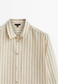 Chemise à manches longues avec des rayures verticales beige et blanches, fermeture boutonnée à l'avant, col pointu sur fond blanc.