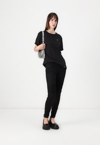 Black t-shirt with short sleeves and a small logo, paired with black pants featuring ribbed detailing, and chunky black shoes. Silver handbag.