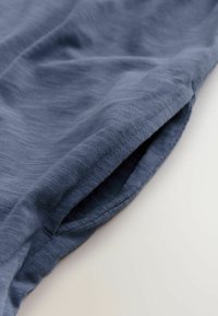 Blauer Stoff mit einer weichen, strukturierten Oberfläche und einem gefalteten Rand. Das Material wirkt leicht und fällt sanft.