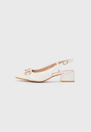 Hvit patentlæder slingback-sko med blokhæl og guldbeslagdetalje på spidse tå mot en plain baggrund.