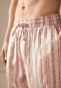 Pantalons de détente légers, rayés, fabriqués en tissu tissé doux dans des tons de rose pâle et de crème, avec une taille élastique et un cordon de serrage.