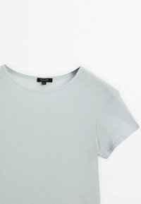 T-shirt en coton bleu clair à manches courtes avec col rond, étalé à plat et montrant l'avant supérieur et la manche droite sur un fond blanc.