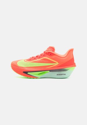 Sapatilha de corrida com um superior laranja brilhante, realces verde neon, design aerodinâmico e uma sola distinta cinza e verde, rotulada "ZOOMX."