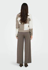 Maglione corto in beige e crema, caratterizzato da motivi testurizzati, abbinato a pantaloni larghi grigi a gamba larga. Materiali morbidi e accoglienti.