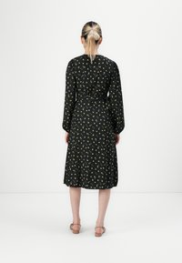 Black patterned dress with yellow floral details, long sleeves, and a tie at the waist. Fabric appears soft with a flowing shape.