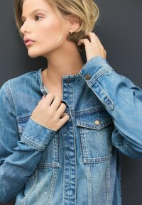 Lichtblauwe denimjas met een drukknoopsluiting, puntige kraag en borstzakken. Heeft een relaxte pasvorm en zichtbare stikseldetails.