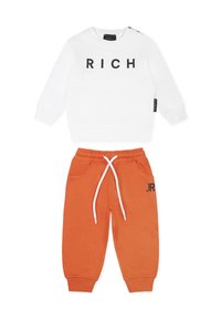 Biała bluza z czarnym napisem "RICH" i bocznymi guzikami, zestawiona z pomarańczowymi spodniami dresowymi z białym sznurkiem i czarnym logo "JR".
