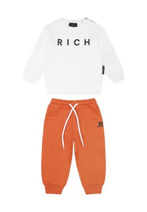 Biała bluza z czarnym napisem "RICH" i bocznymi guzikami, zestawiona z pomarańczowymi spodniami dresowymi z białym sznurkiem i czarnym logo "JR".