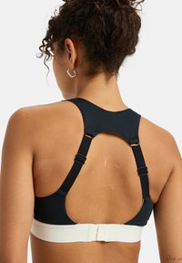 Black sports bra with a wide white band, adjustable straps, and a racerback design. Smooth material with minimal stitching visible.