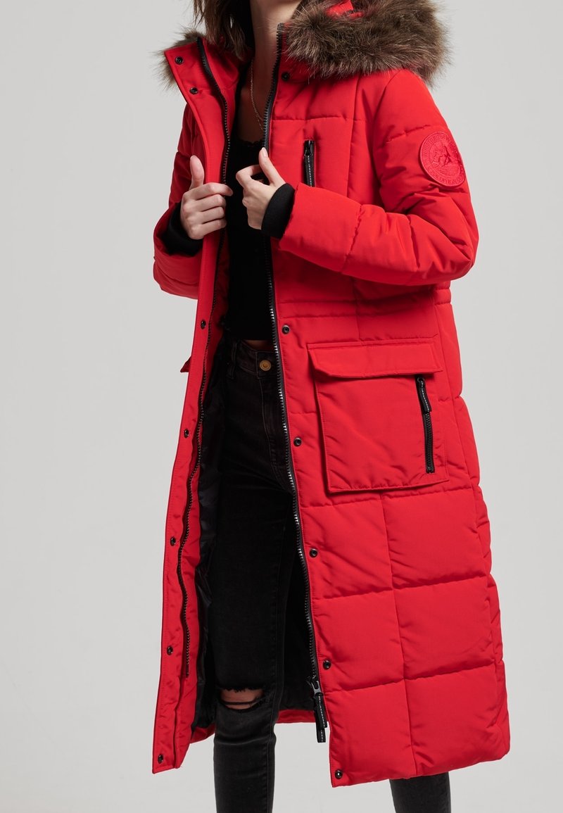 Rode lange pufferjas met een met bont gevoerde capuchon, ritszakken, gestikte textuur en een voorzijde met rits. Casual kleding met een relaxte pasvorm.