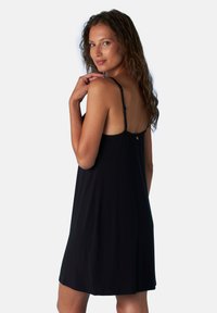 Abito nero senza maniche con vestibilità rilassata, dotato di spalline sottili e un dettaglio con bottoni sulla parte posteriore. Texture liscia e lunghezza fino a metà coscia.