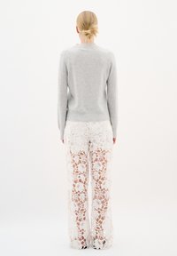 Pulover gri și pantaloni din dantelă albă. Puloverul are un decolteu rotund și mâneci lungi. Pantalonii au modele florale din dantelă și o textură transparentă.
