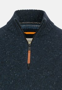 Granatowy sweter wykonany na drutach z wysokim kołnierzem i zapięciem na zamek. Teksturowany materiał z delikatnymi plamkami. Skórzana dekoracja na suwaku.