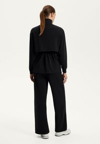 Zwart tweedelig outfit met een colbert, lange mouwen en een geraffineerde taille, gecombineerd met wijde broekspijpen. Glad materiaal, minimalistisch ontwerp.
