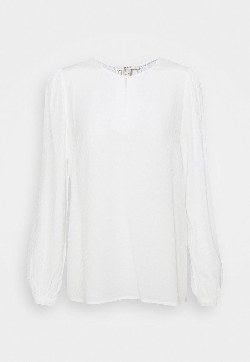 Blouse blanche à manches longues en tissu subtilement texturé, col rond et manches légèrement bouffantes terminées par des poignets.