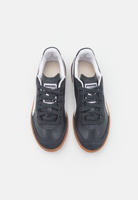 Paire de baskets noires et blanches à lacets avec semelles en caoutchouc marron vues de dessus sur fond blanc.