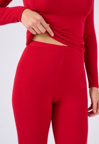 Rotes langärmliges Oberteil, kombiniert mit passenden roten Leggings, beide aus einem weichen, dehnbaren Stoff. Die Leggings verfügen über einen nahtlosen Bund.