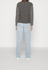 Camisa de manga larga a rayas en blanco y negro combinada con vaqueros de pierna ancha en azul claro y zapatillas blancas con detalles en azul.