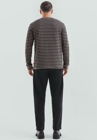 Gestreepte lange mouwen shirt in bruintinten, met donkere strepen. Gepaarde met zwarte broek en schoenen, met een ontspannen silhouet.