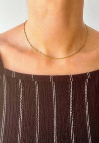 Gold-tone twisted necklace resting on bare skin, paired with a dark striped top featuring white accents. Simple and delicate design.