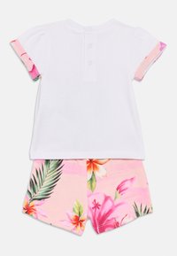 Λευκό τοπ με κοντά μανίκια και κλείσιμο με κουμπιά στο πίσω μέρος· ροζ σορτς με λουλουδάτο σχέδιο που περιλαμβάνει ιβίσκο και φύλλα φοίνικα.