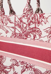 Stof tas med et rødt blomstermønster og dyremotiv på en lys baggrund, med horisontale striber i varierende nuancer af pink.