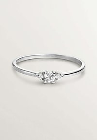 Anillo de plata con tres diamantes redondos: una piedra central flanqueada por dos piedras más pequeñas, acabado pulido, banda delgada.