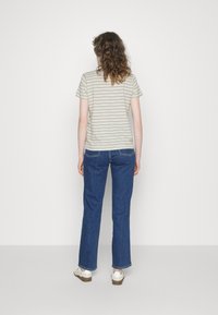 Randig kortärmad t-shirt i ljus beige och grå, ihop med blå rakbenade jeans och vita sneakers. Enfärgad bakgrund.