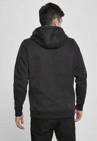 Felpa nera con cappuccio caratterizzata da un tessuto testurizzato, polsini e orlo a coste, con cappuccio regolabile tramite cordino. La parte posteriore presenta un design minimalista.