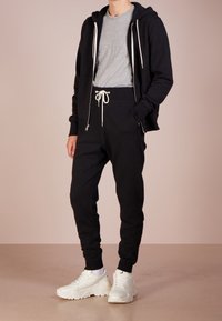 Czarna bluza z zamkiem, szary T-shirt, czarne spodnie dresowe z białym sznurkiem i białe trampki. Miękka tkanina, luźny krój, minimalistyczny design.
