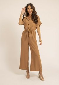 Jumpsuit marron à manches courtes avec col, fermeture à boutons et taille nouée. Design à jambes larges, tissu texturé et coupe décontractée.