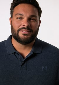 Marinblå polo skjorta med tre knappar, texturerad tyg, med en diskret präglad logotyp på vänster bröst. Standard kragsdesign.